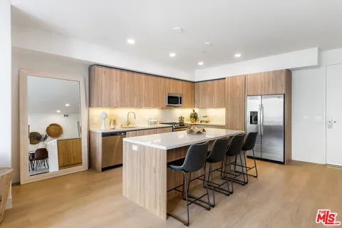 a kitchen with stainless steel appliances granite countertop a center island a stove a refrigerator and a dining table with wooden floor