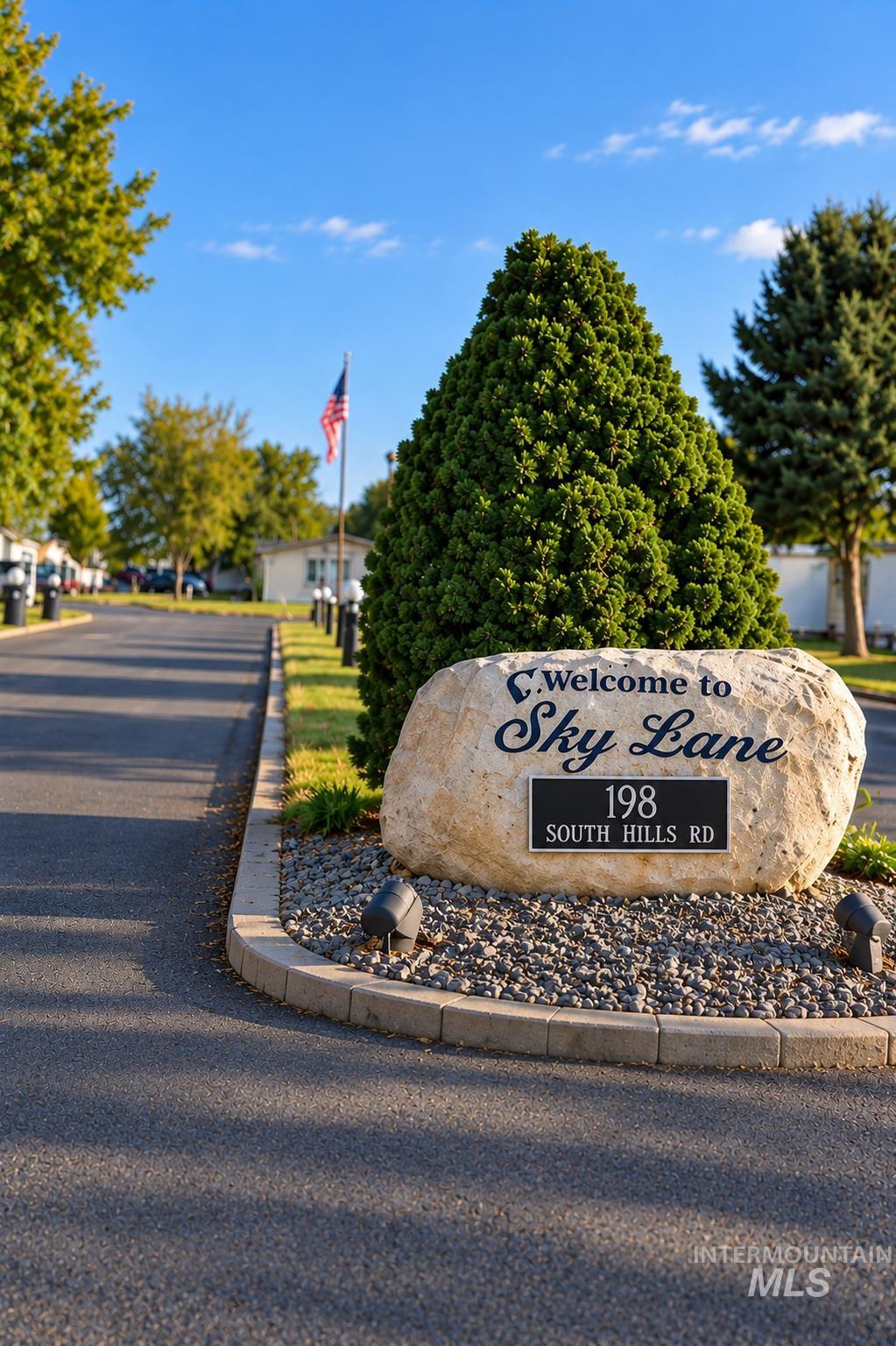 198 South Hills Road, Unit 52 Twin Falls, ID 83301 - Photo 22 of 22 Stone monument sign featuring a dark plaque, set in a gravel bed with landscape lighting, bordered by a concrete curb