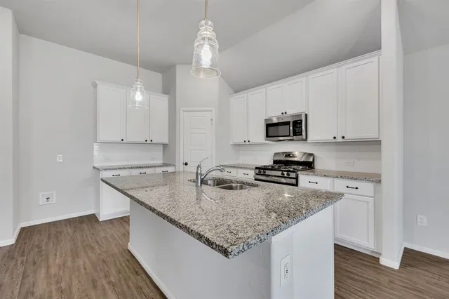 a kitchen with granite countertop a sink dishwasher stove and microwave with wooden floor