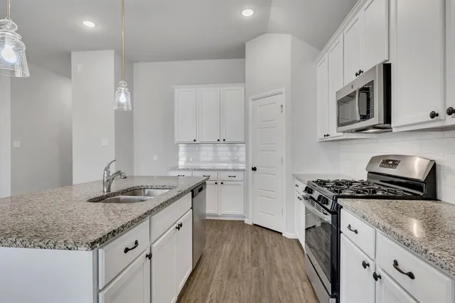 a kitchen with stainless steel appliances granite countertop a sink stove oven and white cabinets with wooden floor