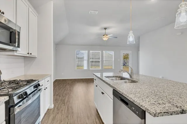 a kitchen with granite countertop stainless steel appliances a sink cabinets and wooden floor