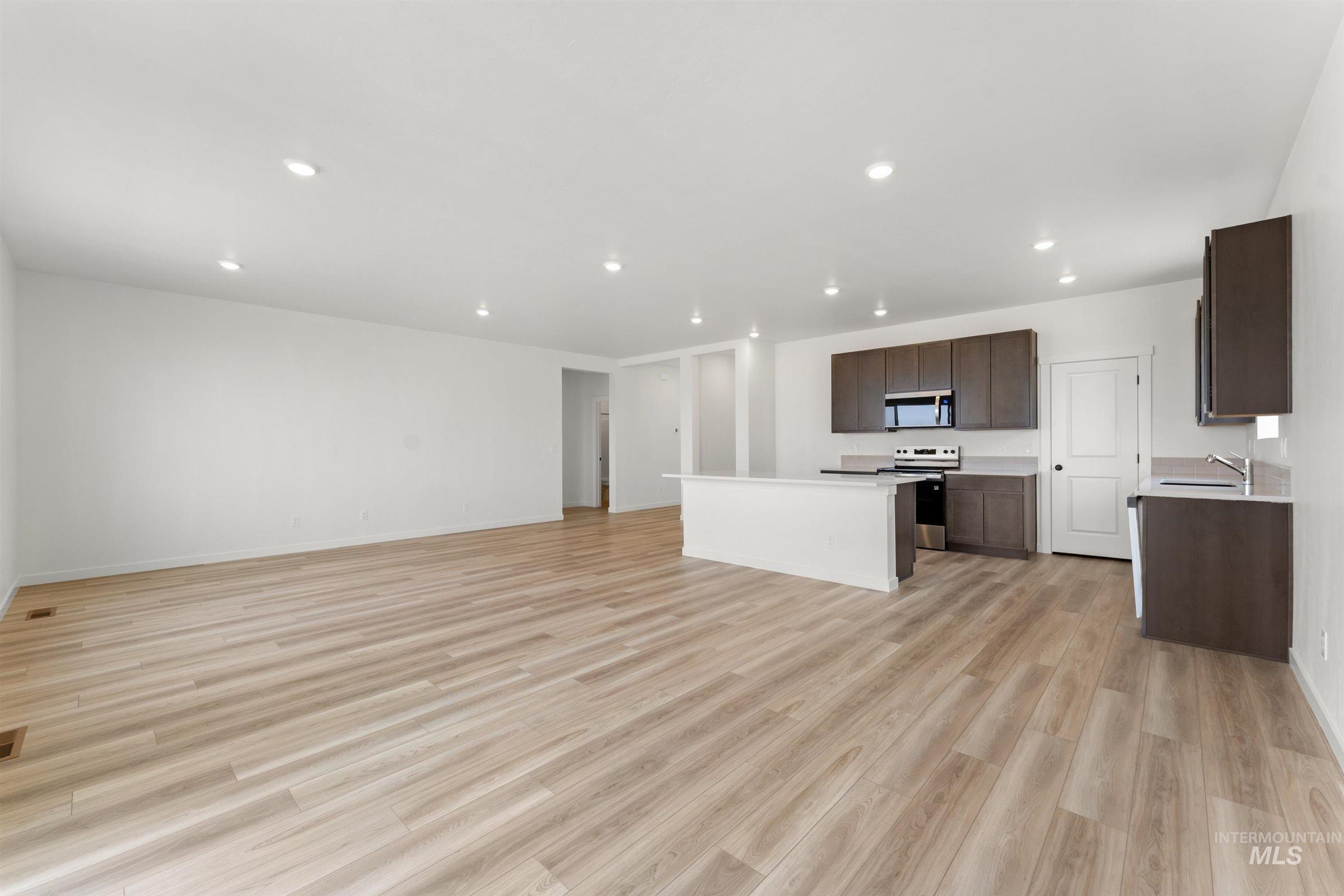 1076 East Exploration Drive Kuna, ID 83634 - Photo 28 of 29 Kitchen featuring open floor plan, light countertops, dark brown cabinets, appliances with stainless steel finishes, and light wood-style flooring