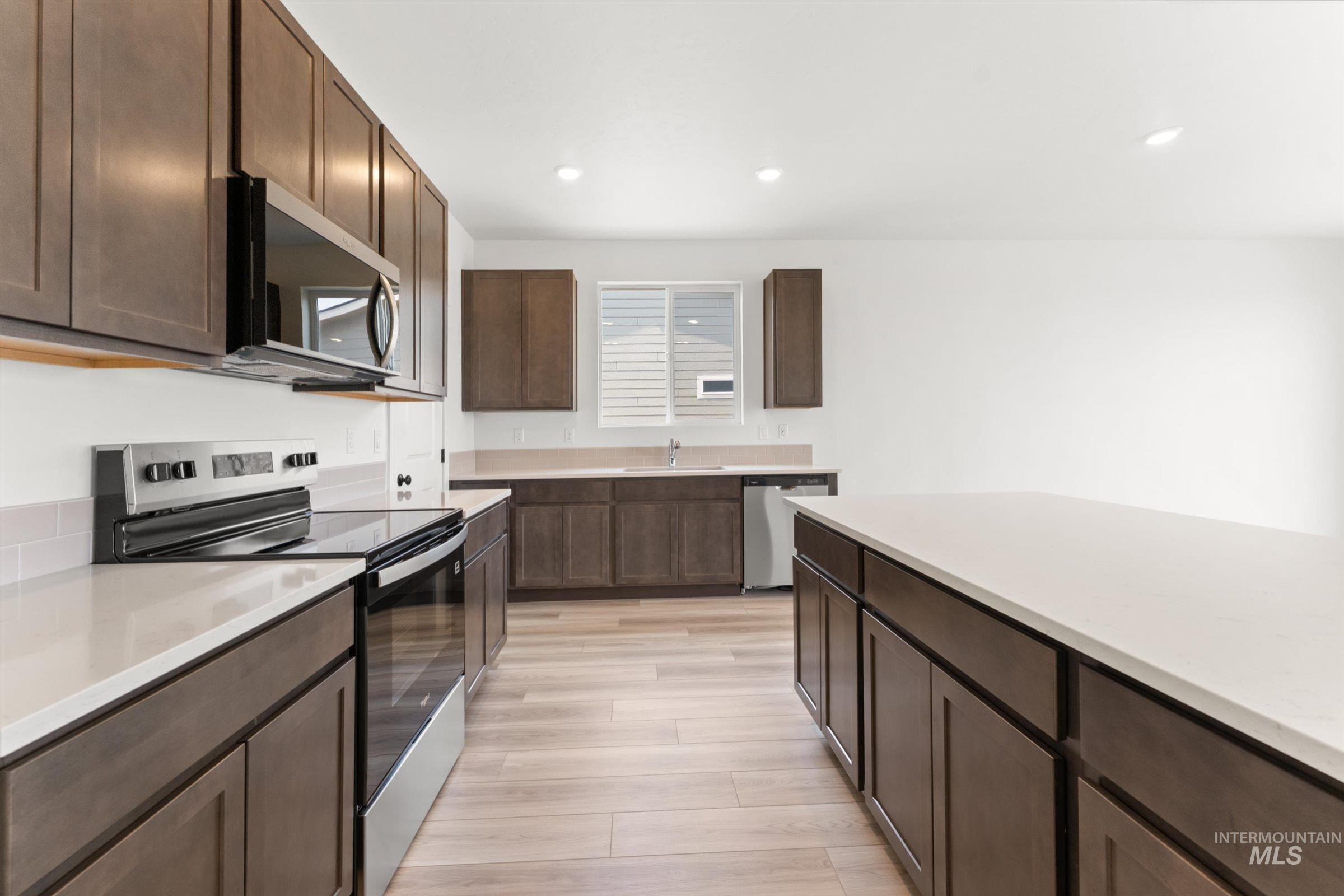 1076 East Exploration Drive Kuna, ID 83634 - Photo 5 of 29 Kitchen featuring stainless steel appliances, dark brown cabinets, recessed lighting, light wood-style floors, and light stone countertops
