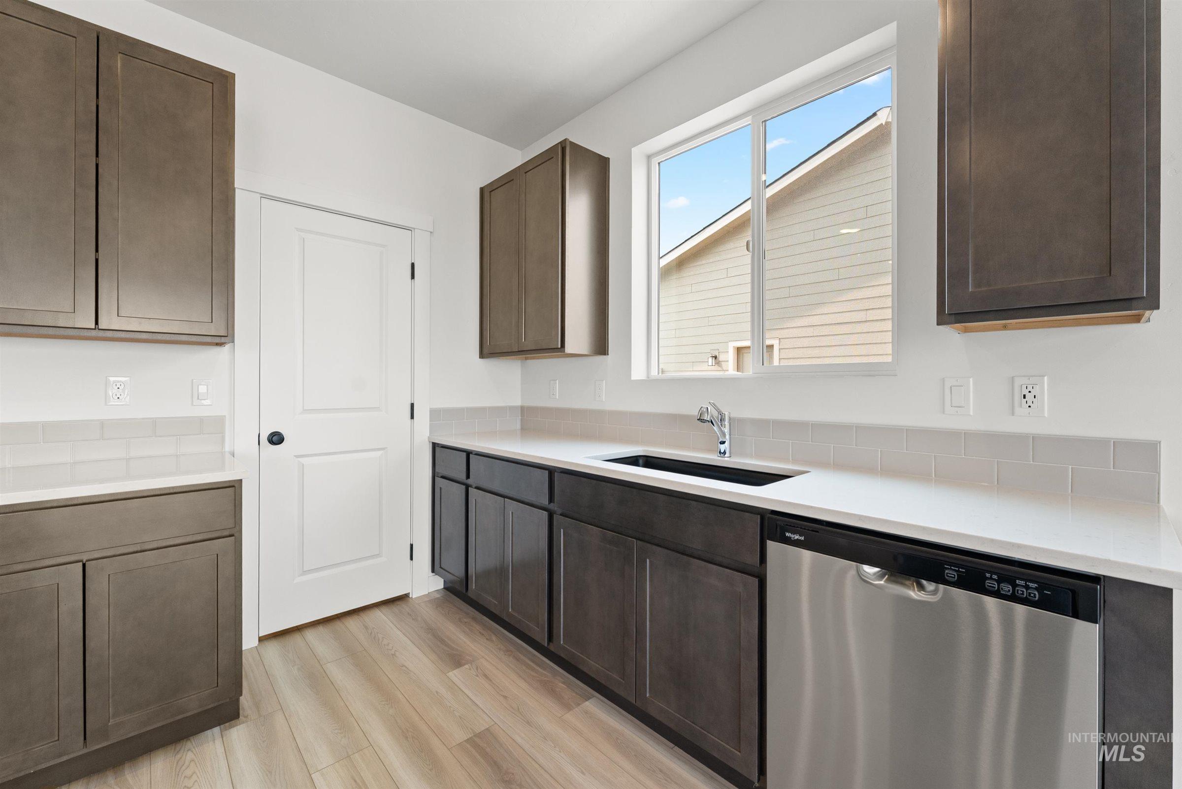 1076 East Exploration Drive Kuna, ID 83634 - Photo 6 of 29 Kitchen featuring dishwasher, dark brown cabinetry, light wood-type flooring, and light stone countertops
