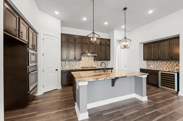 a kitchen with stainless steel appliances kitchen island granite countertop a refrigerator a stove and a wooden floor