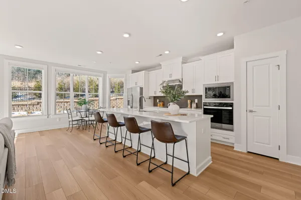 a kitchen with stainless steel appliances granite countertop a stove top oven a refrigerator a dining table and chairs with wooden floor