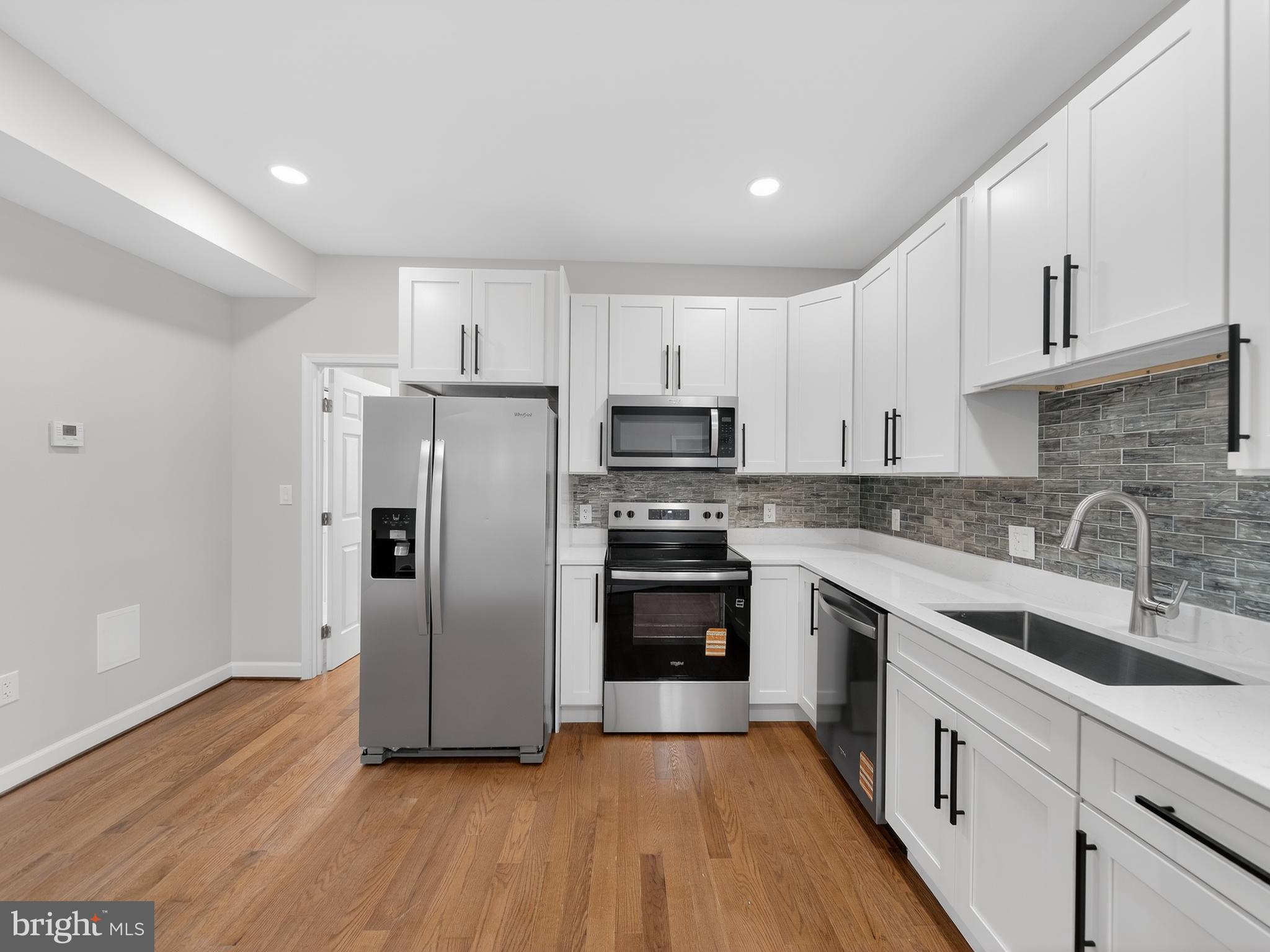 a kitchen with stainless steel appliances granite countertop a refrigerator a sink dishwasher a stove oven and white countertops with wooden floor