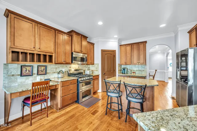 a kitchen with stainless steel appliances granite countertop a stove top oven a refrigerator a dining table and chairs with wooden floor