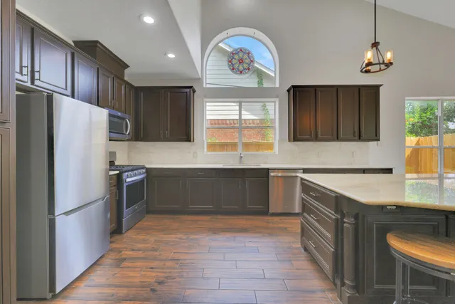 a kitchen with stainless steel appliances granite countertop a refrigerator a sink dishwasher a stove with wooden floor and cabinets