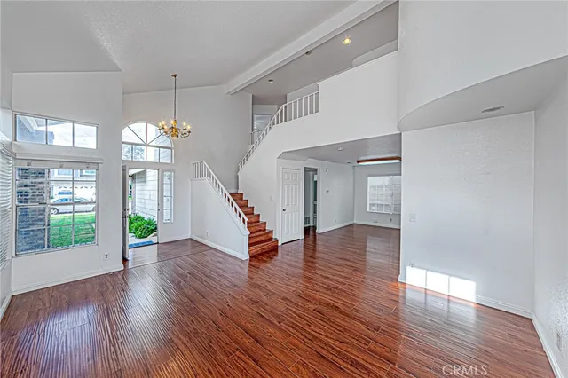 an empty room with wooden floor chandelier and windows