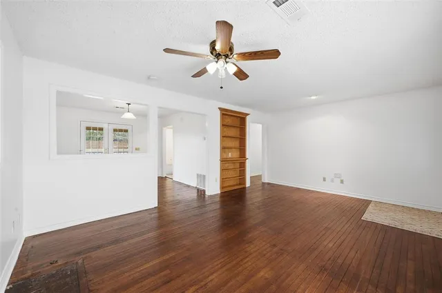 a view of an empty room with wooden floor and a ceiling fan