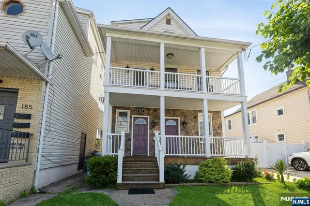 a view of a white house with large windows and a small yard plants and large tree