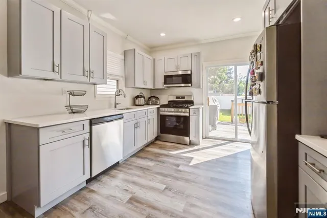 a kitchen with stainless steel appliances granite countertop a stove top oven a sink a refrigerator white cabinets and wooden floor