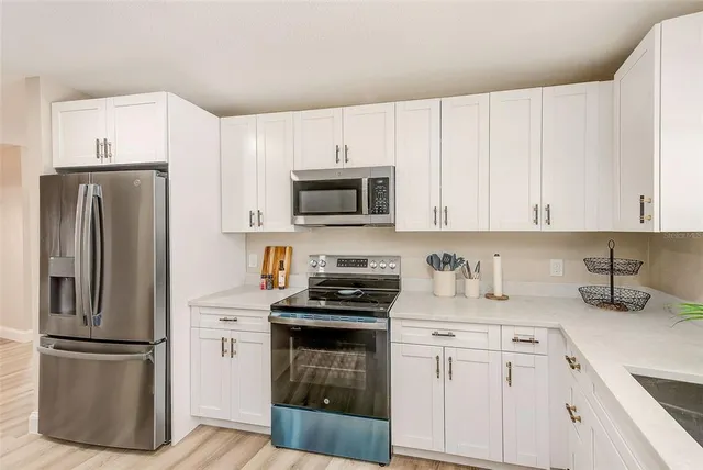 a kitchen with stainless steel appliances white cabinets a sink dishwasher and a stove with wooden floor