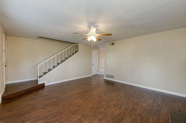 a view of an empty room with wooden floor and a ceiling fan