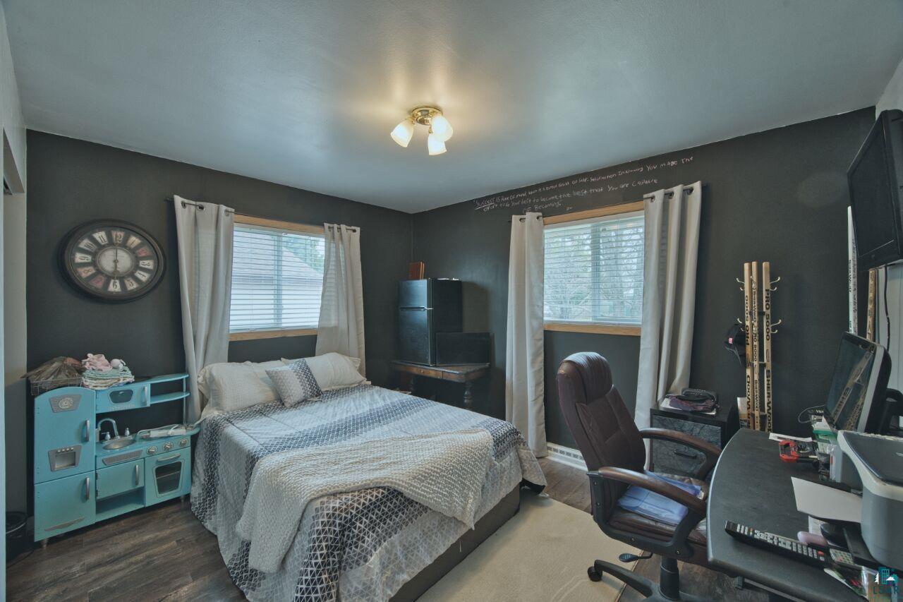 329 Wyandotte Road Hoyt Lakes, MN 55750 - Photo 13 of 52 Bedroom featuring dark wall paint, wood-finish flooring, two windows with blinds, and an overhead light fixture