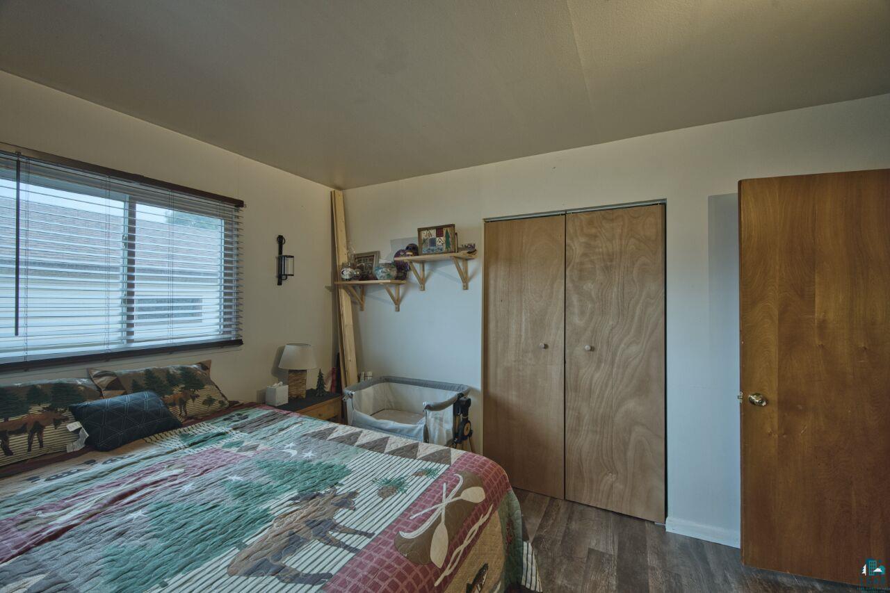 329 Wyandotte Road Hoyt Lakes, MN 55750 - Photo 17 of 52 Bedroom featuring a window with horizontal blinds, wood-finish flooring, bi-fold closet doors, and a wood-paneled door