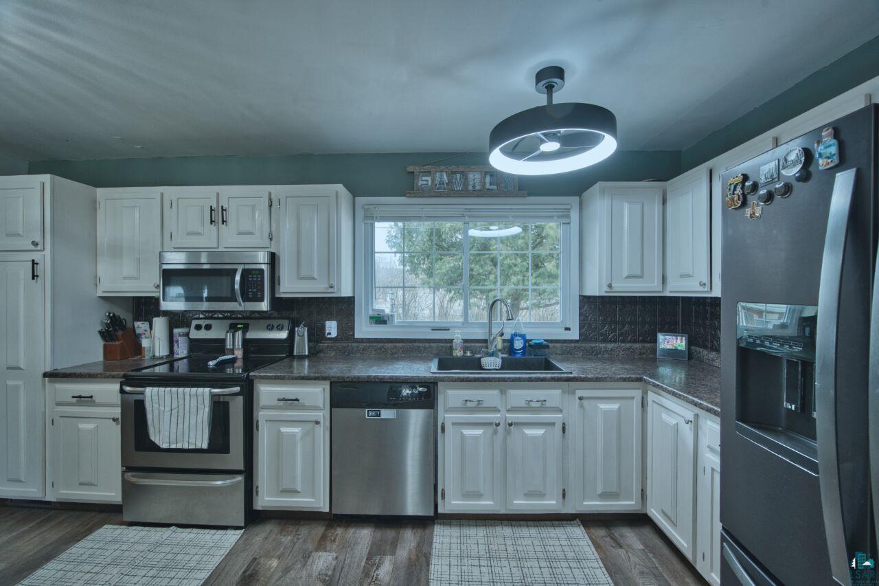 329 Wyandotte Road Hoyt Lakes, MN 55750 - Photo 2 of 52 Kitchen featuring white cabinetry, stainless steel appliances, dark countertops, dark tile backsplash, and wood-finish flooring