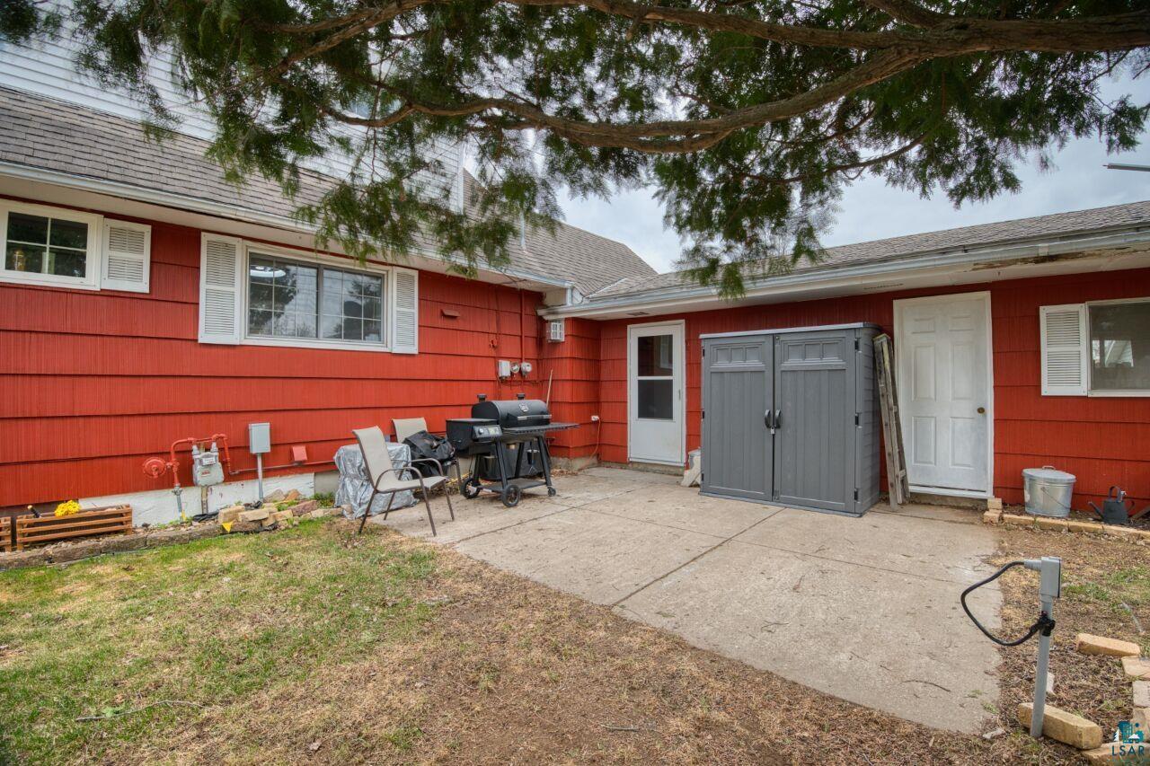 329 Wyandotte Road Hoyt Lakes, MN 55750 - Photo 35 of 52 Exterior featuring red siding, multiple windows with white shutters, a concrete patio, and a storage shed