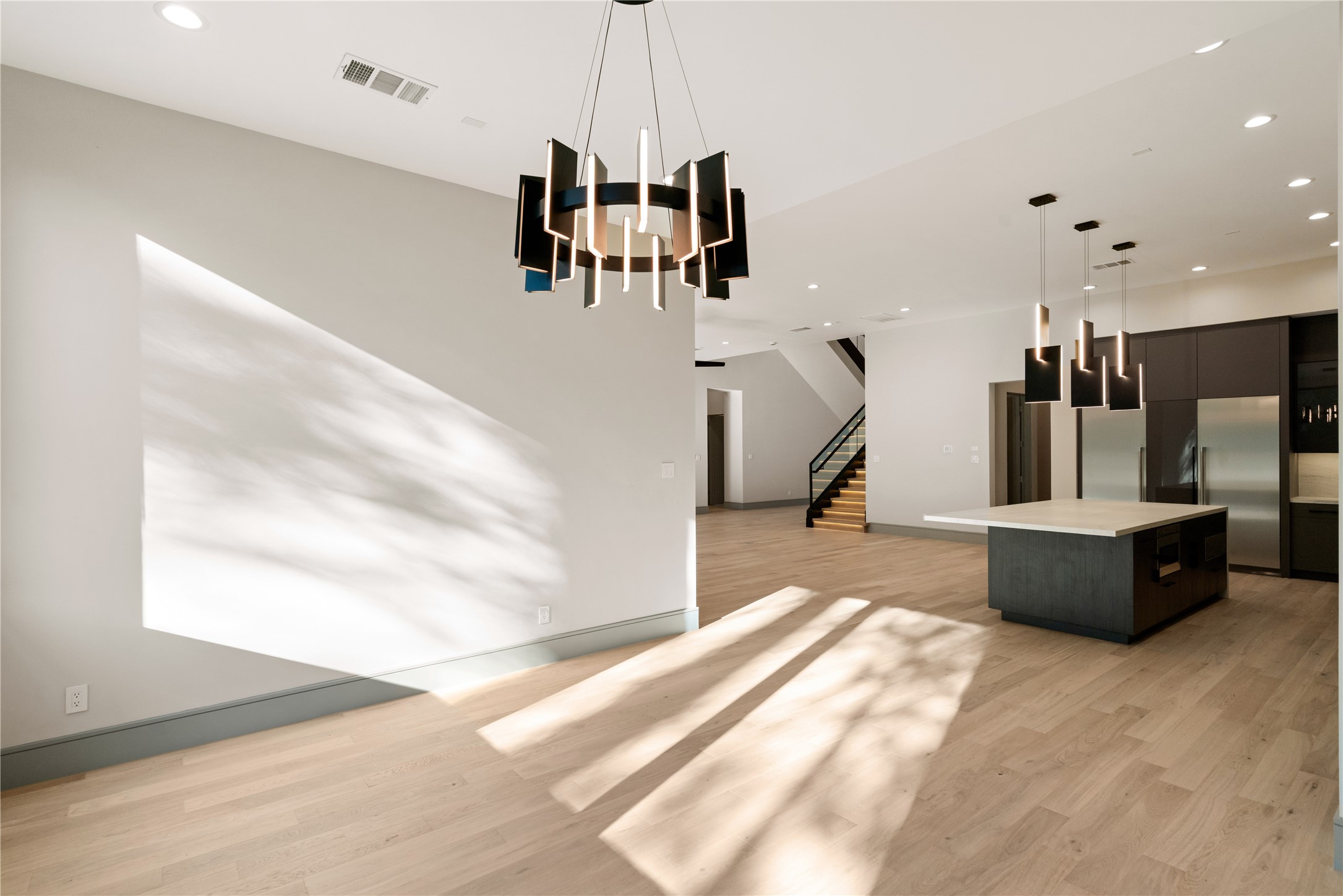 47 Pronghorn Place Spring, TX 77389 - Photo 14 of 44 This modern open-concept living space features sleek lighting fixtures, light wood flooring, and ample natural light. The kitchen includes a large island and stainless steel appliances, while the area leads to a staircase with a contemporary design.