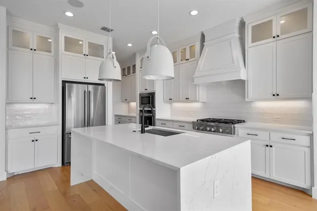 a kitchen with stainless steel appliances granite countertop a sink a stove a refrigerator and white cabinets
