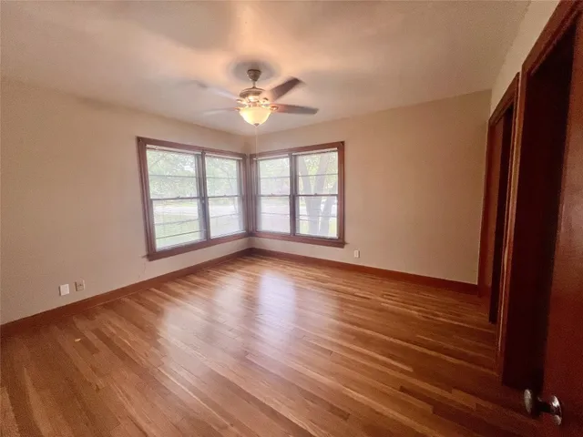 an empty room with wooden floor chandelier fan and windows