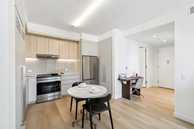 a kitchen with stainless steel appliances kitchen island granite countertop a dining table chairs and a refrigerator