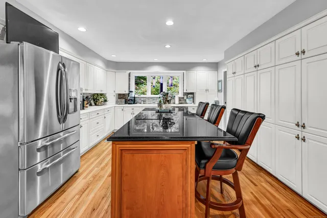 a kitchen with stainless steel appliances granite countertop a refrigerator a sink dishwasher a dining table and chairs with wooden floor