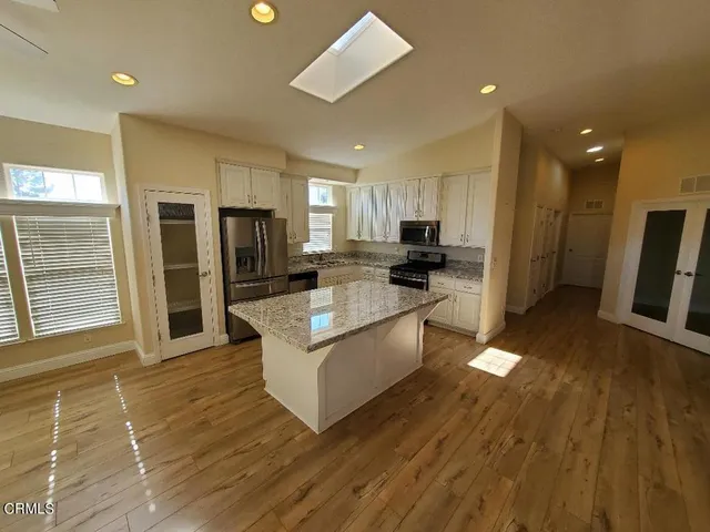 a kitchen with stainless steel appliances granite countertop a refrigerator a sink dishwasher a stove and white countertops with wooden floor