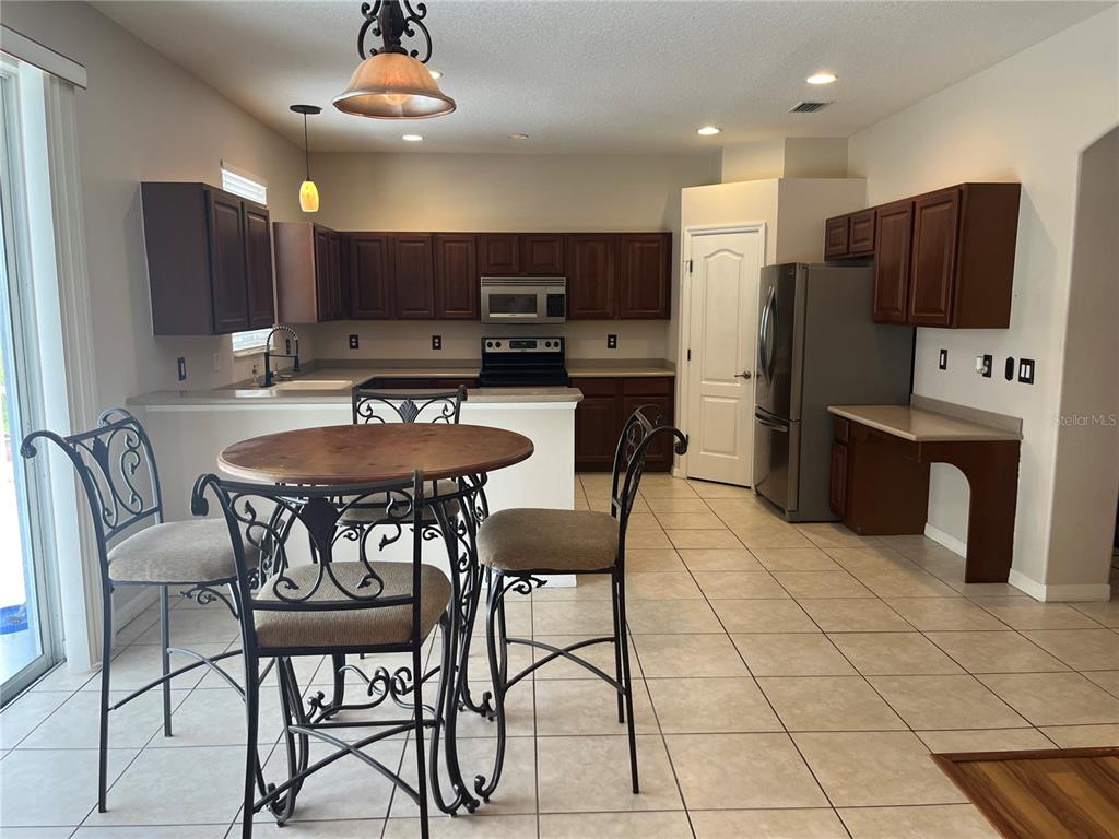 5966 Willows Bridge Loop Ellenton, FL 34222 - Photo 13 of 57 a kitchen with stainless steel appliances kitchen island granite countertop a table chairs and a refrigerator