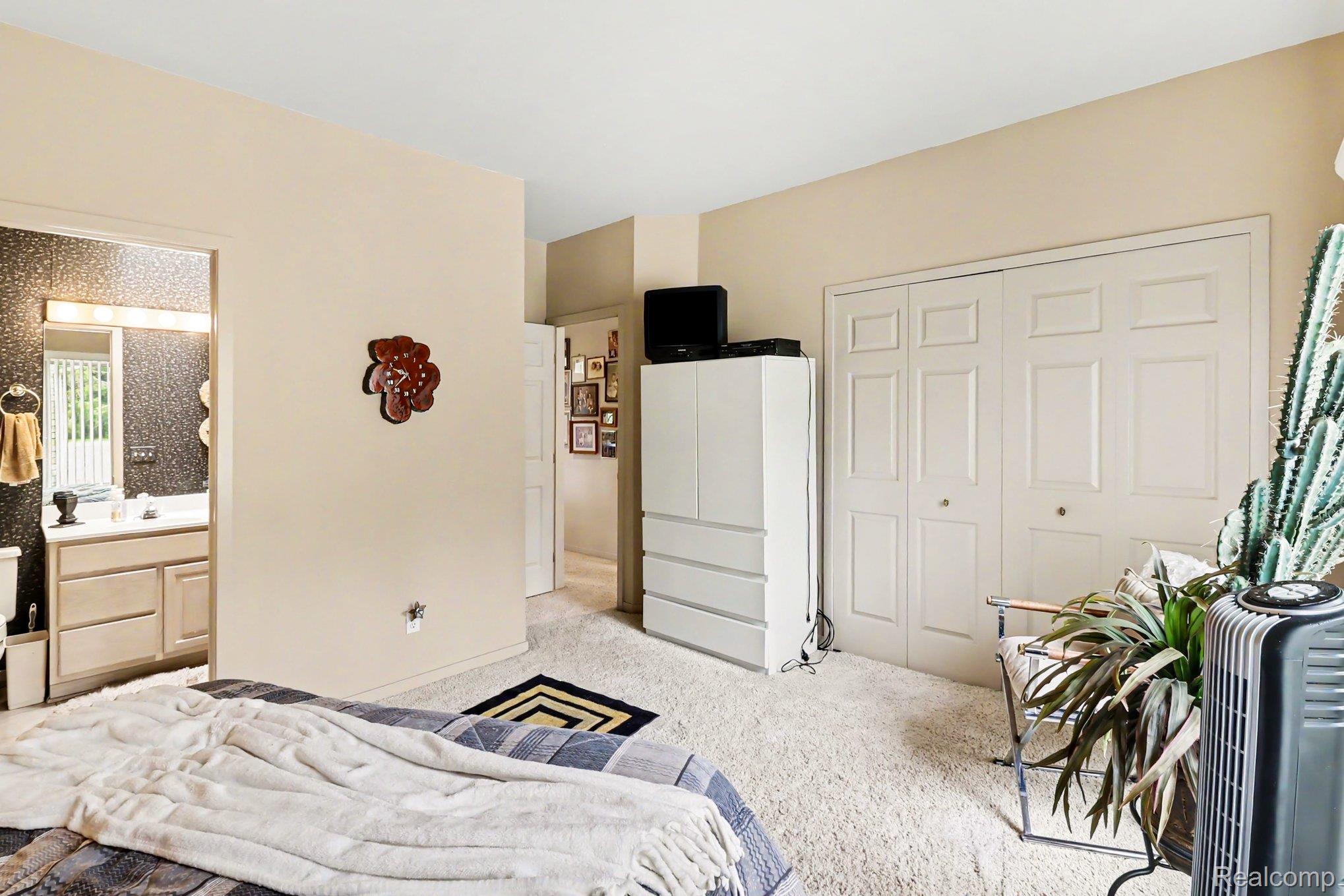 18501 Taylor Lake Road Holly, MI 48442 - Photo 21 of 35 Carpeted bedroom featuring neutral-toned walls, bi-fold closet doors, and an open doorway revealing a bathroom vanity with a mirror and light fixture