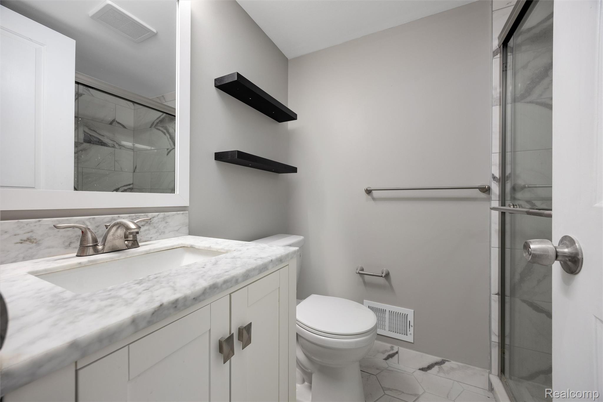 4942 Butler Drive Troy, MI 48085 - Photo 15 of 33 Bathroom featuring a white vanity with an integrated sink and stone countertop, brushed nickel faucet, a glass-enclosed shower with stone-look tile, and hexagonal stone-look floor tiles