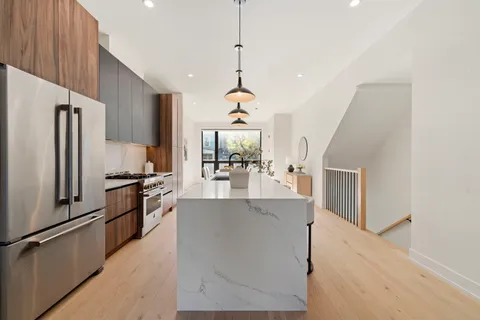 a kitchen with stainless steel appliances granite countertop a refrigerator a oven a stove and a dining table with wooden floor