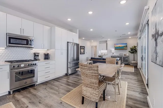 a kitchen with stainless steel appliances a stove a sink a refrigerator white cabinets and wooden floor