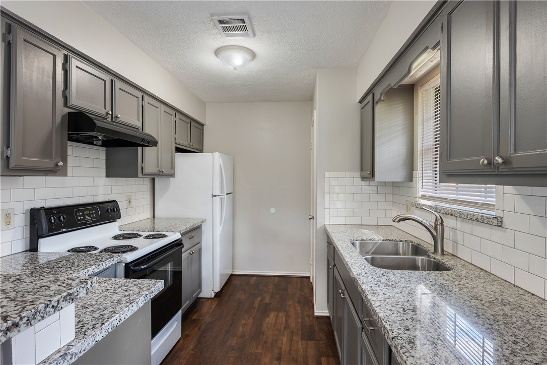 Kitchen with electric range oven, gray cabinets, dark wood-type flooring, under cabinet range hood, and backsplash