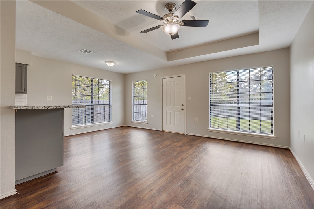 1003 East 24th Street Bryan, TX 77803 - Photo 10 of 24 Unfurnished living room featuring a raised ceiling, plenty of natural light, and dark wood-style flooring