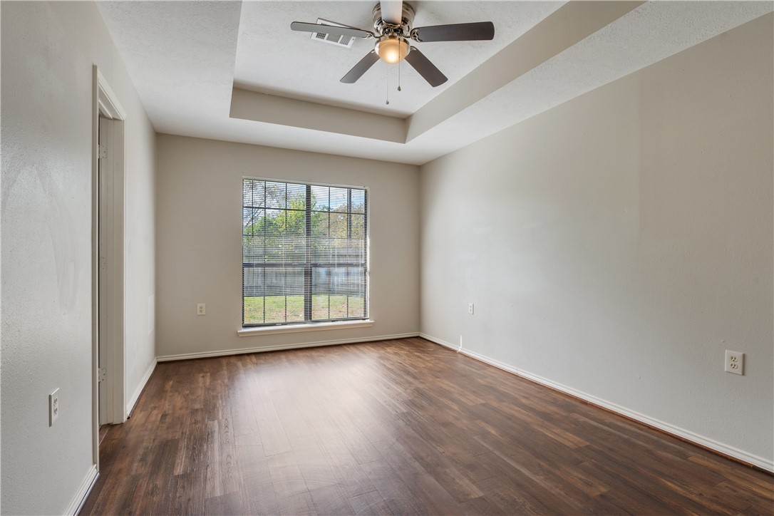 1003 East 24th Street Bryan, TX 77803 - Photo 11 of 24 Empty room with a raised ceiling, dark wood-style flooring, and ceiling fan