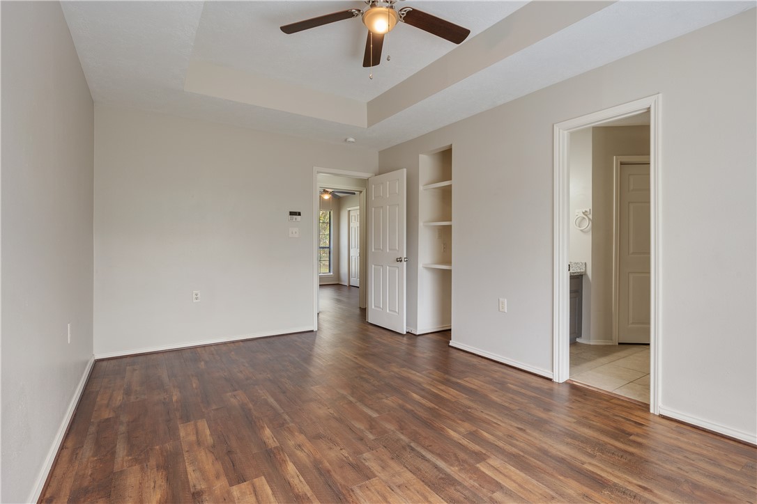 1003 East 24th Street Bryan, TX 77803 - Photo 12 of 24 Unfurnished bedroom featuring dark wood finished floors, a raised ceiling, ceiling fan, and connected bathroom