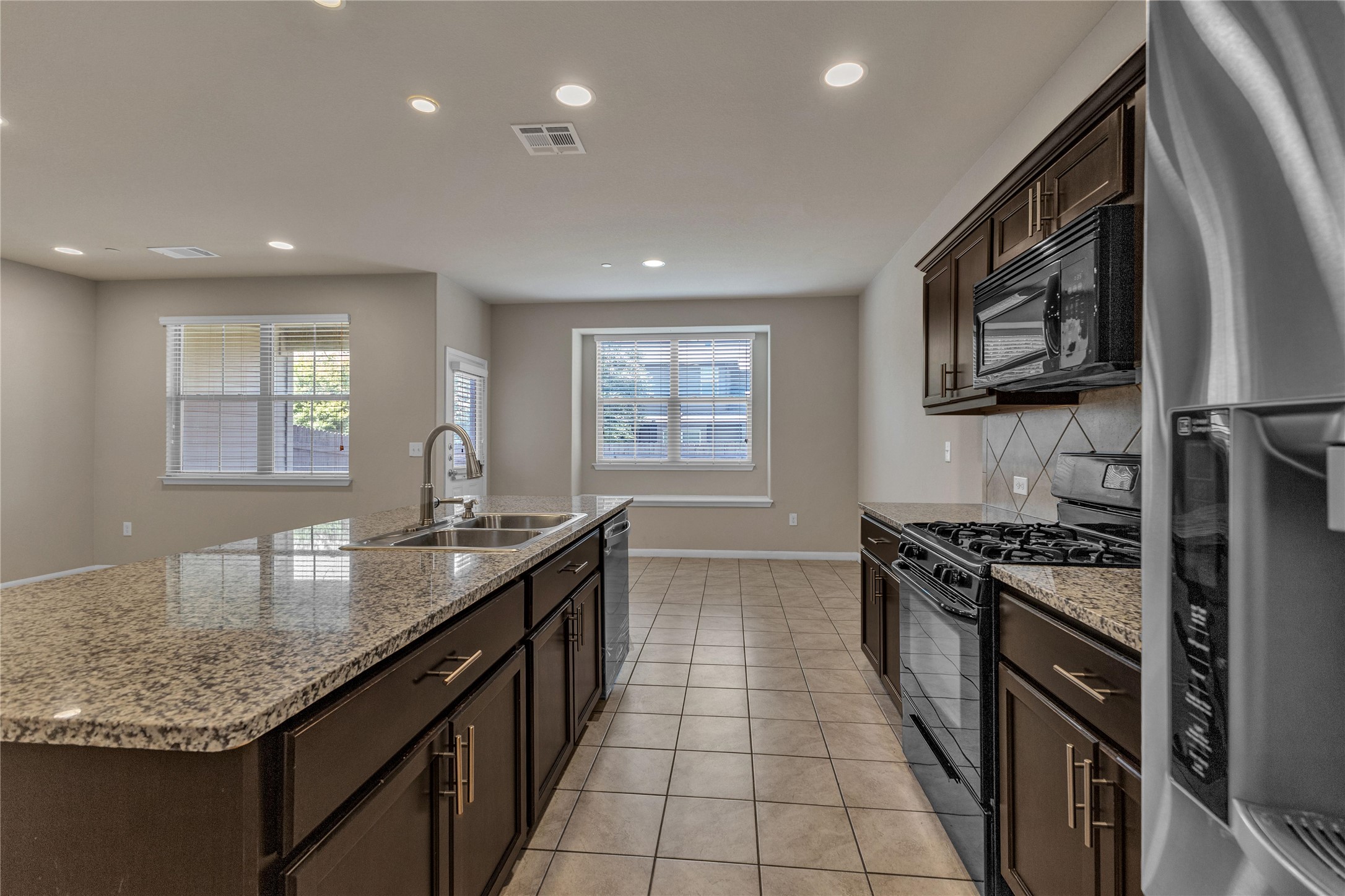 2880 Donnell Drive, Unit 2003 Round Rock, TX 78664 - Photo 11 of 31 Kitchen featuring a central island with a double basin sink and granite-style countertop, dark wood-finish cabinetry, black appliances including a gas range and built-in microwave, and tile flooring
