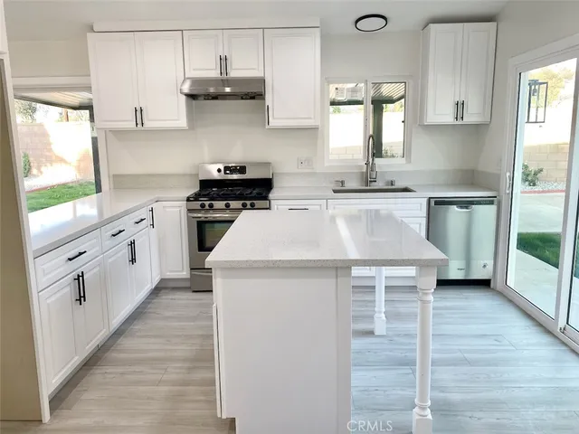 a kitchen with stainless steel appliances a sink a stove and white cabinets with wooden floor