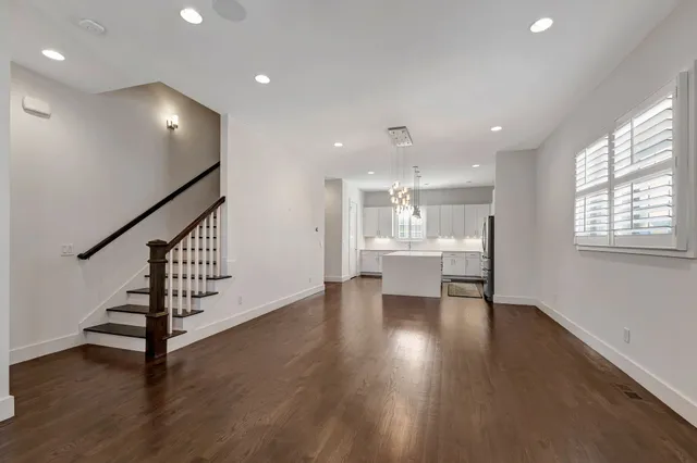 a view of an empty room with wooden floor and a kitchen