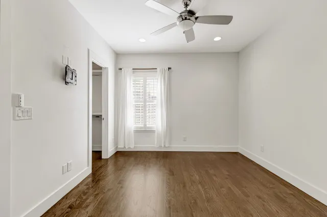 an empty room with wooden floor fan and windows