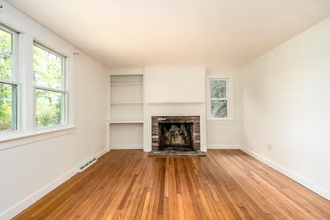 an empty room with wooden floor fireplace and windows
