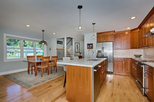 a kitchen with stainless steel appliances granite countertop a stove top oven a sink dishwasher a dining table and chairs with wooden floor