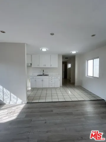 a view of an empty room and kitchen view with wooden floor