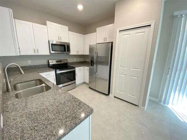 a kitchen with stainless steel appliances granite countertop a refrigerator a stove a sink and white cabinets