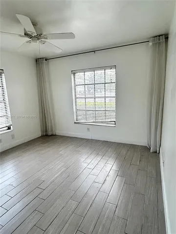 an empty room with wooden floor fan and windows