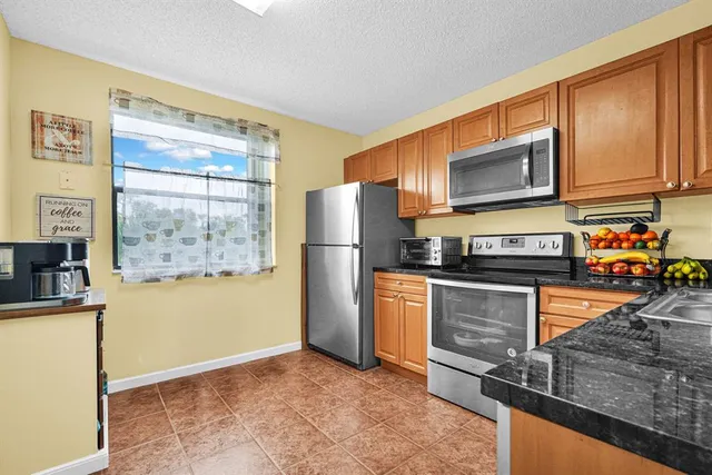 a kitchen with stainless steel appliances granite countertop a refrigerator a stove top oven cabinets a sink and a window