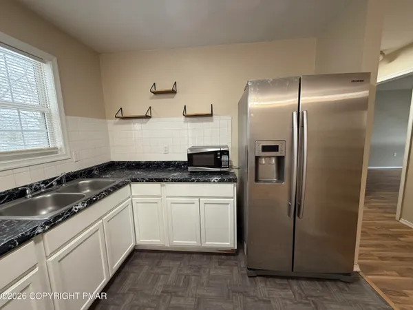 an empty room with wooden floor kitchen view and a windows