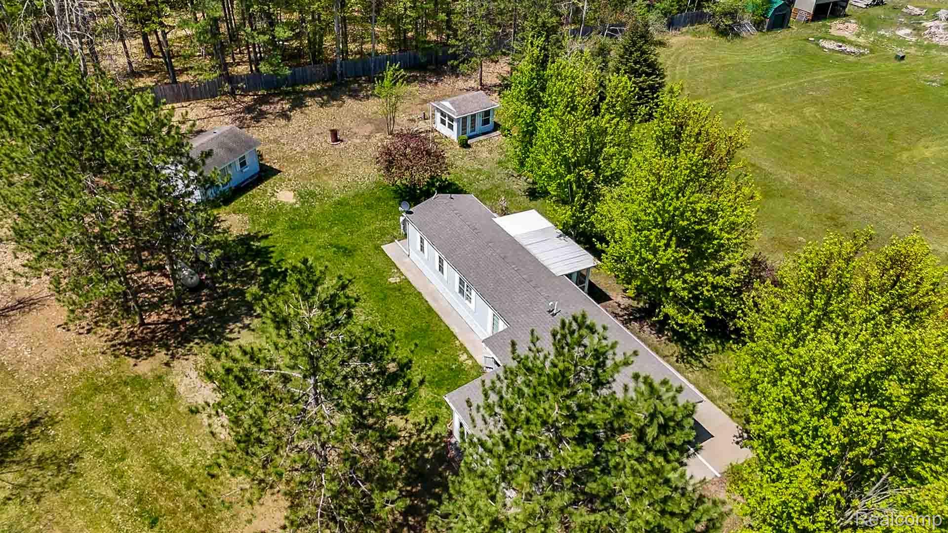 1094 Blamer Road Fairview, MI 48621 - Photo 86 of 97 Expansive property featuring a light blue siding residence with a dark gray roof, surrounded by mature trees, a manicured lawn, and two additional outbuildings